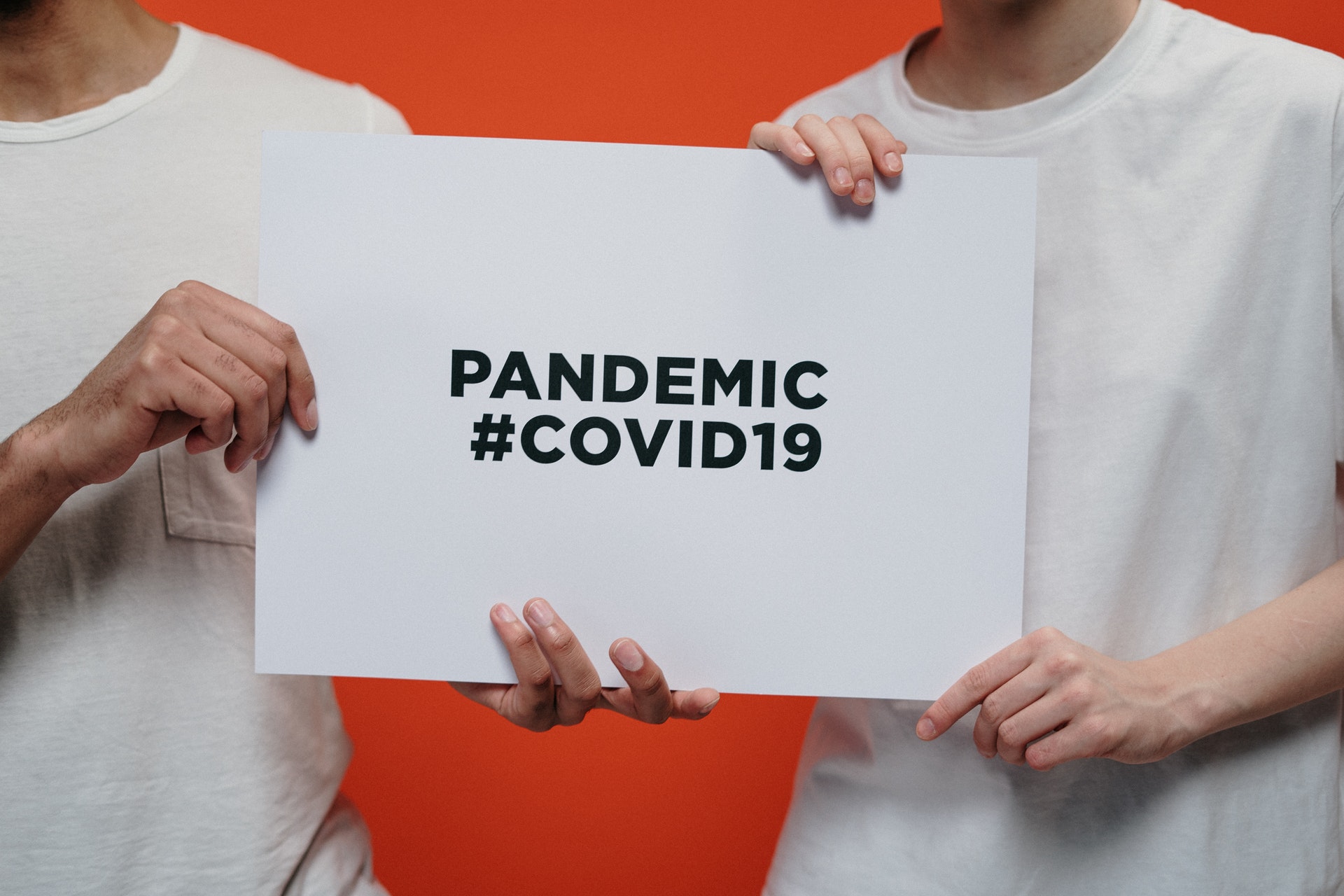 Two persons holding a placard with "PANDEMIC #COVID19"